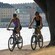 2 people riding bicycles on a tree lined path next to the water
